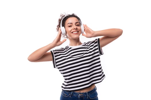 young positive curly brunette woman in a striped casual t-shirt listens to music in headphones.