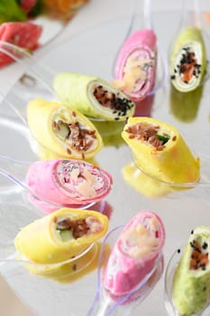 Cheese appetizer in rolls on small disposable spoons, roll in purple and yellow colors.