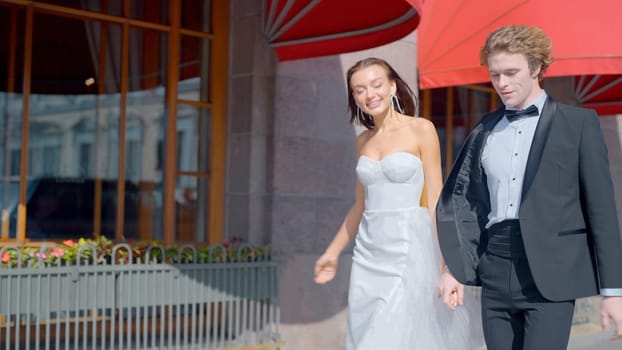 Wedding photo shoot on the street.Action.A bright and spectacular couple with a bride in a white dress with a neckline and long earrings and a man in a black suit on the street next to buildings. High quality 4k footage