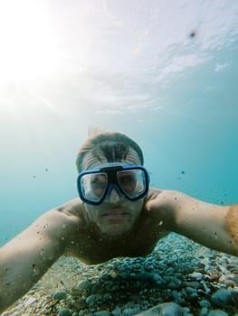 Diver in snorkeling goggles swims above the sea pebble bottom. High quality photo