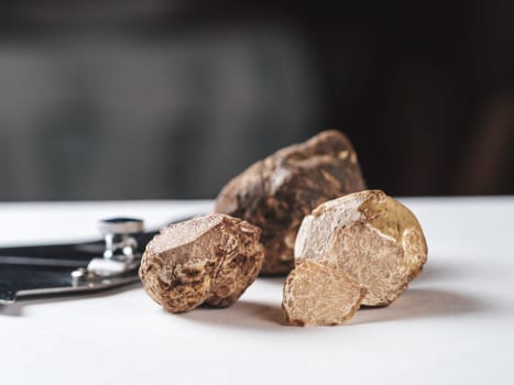 Expensive white truffles gourmet mushrooms on white table in restaurant interior. Row of brown truffles with slice on a white table with dark background. Truffle mushrooms is culinary delight. Close up. Macro.