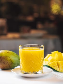 Mango fresh juice in restaurant interior. Yellow mango shake served for drink. Hot day refreshing beverage. Sweet mango juice in glass. Glass of fresh yellow mango cocktail or juice, vertical with copy space