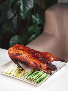 Oven roasted duck - whole baked duck with fresh green cucumber and onion. Whole Peking duck on restaurant table. Peking duck is Traditional Chinese Dish