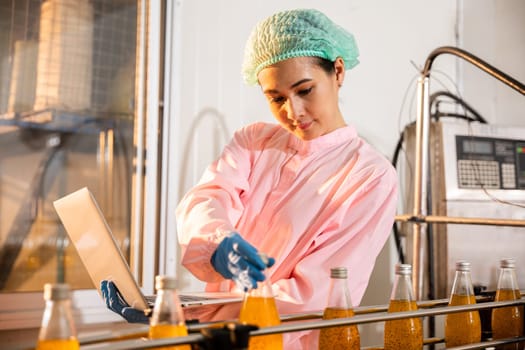 A female engineer oversees beverage bottles on a conveyor belt in the factory. Employing a laptop she guarantees liquid quality adhering to industry standards.