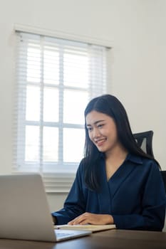 Happy young woman asian working from home distance on laptop taking notes. Smiling business woman lady using computer watching webinar sit on desk writing in notebook.