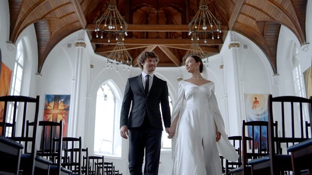 A couple of newlyweds walking quickly through the temple. Action.A beautiful bride in a white tight dress and a veil with a man in a suit with a beard are running with a quick gait through the church hall. High quality 4k footage