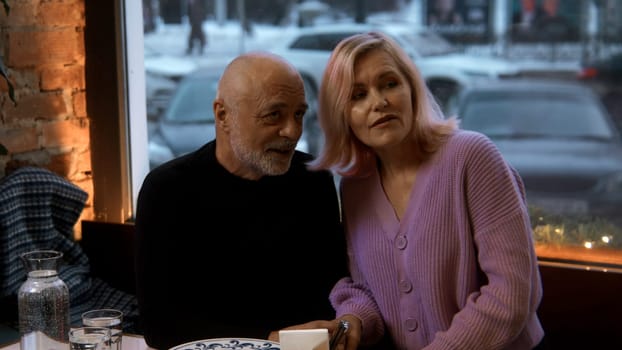 Happy middle aged mature couple talking eat a cafe on a date. Stock footage. Blonde woman pointing finger and speaking