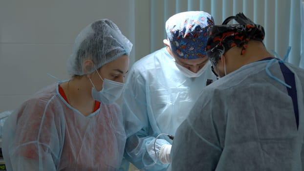 Group of surgeons working in operating room at hospital. Action. Nurse helping two doctors during surgery