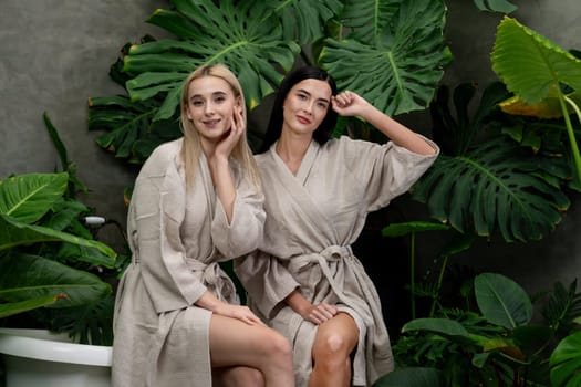 Tropical and exotic spa garden with bathtub in modern hotel or resort with young two women in bathrobe enjoying leisure and wellness lifestyle surrounded by lush greenery foliage background. Blithe