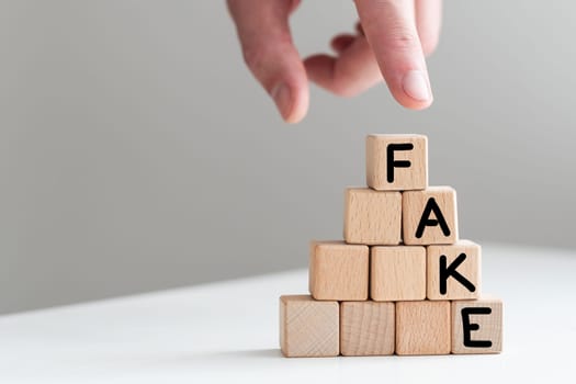 A man in a blue shirt composes the word FAKE from wooden cubes vertically. High quality photo