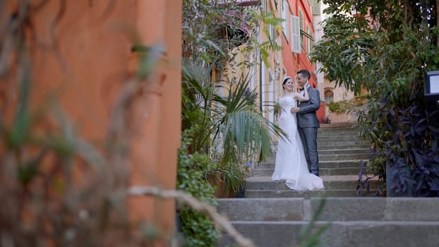 Newlyweds taking pictures on the street. Action. A young couple with a bride in a white dress and a man in a suit who are photographed in full height on the steps next to the architecture of the city. High quality 4k footage