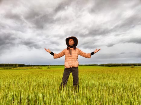 An adult girl looking like a cowboy in a hat in a field and with a stormy sky with clouds takes pictures of rainbow and takes selfie in the rain. Woman having fun outdoors on rural and rustic nature