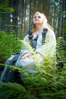 Adult mature woman 40-60 in a green long fairy dress in forest. Photo shoot in style of dryad and queen of nature. Fairy in beautiful green summer forest. Concept of caring for nature