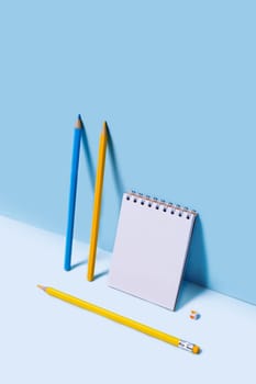 Vertical frontal photo with notebook and pencils leaning against blue wall.