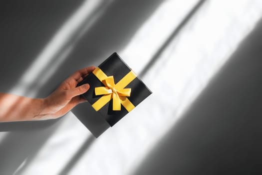 Girl holds gift bandaged with yellow ribbon on gray background. Photo in the colors of the new year.