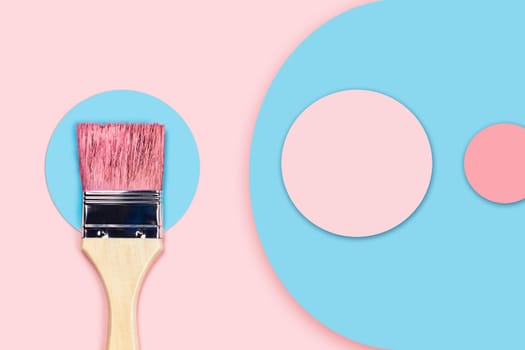 Brush stained with pink acrylic paint lying on a blue paper circle on a pink background. Abstract image.