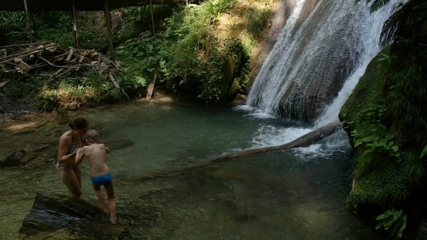 Boy and mother walking among rocks in cold stream. Creative. Hiking in wild nature