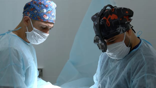 Close up shot of doctor in surgical loupe, sterile mask and protective hair cover looking at the camera. Action. Medical equipment at a hospital