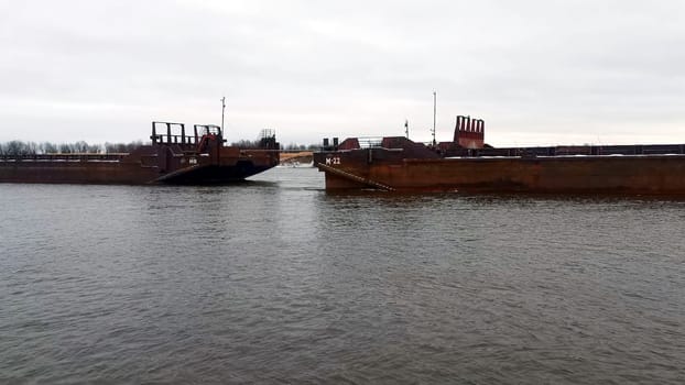 Sea transportation with barges. Clip. Floating barges for cargo transportation on river in winter. Barges on river on cloudy winter day.