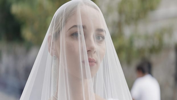 Gorgeous blonde bride with a veil on her face on the background of blurred city street. Action. Wedding day and an elegant woman