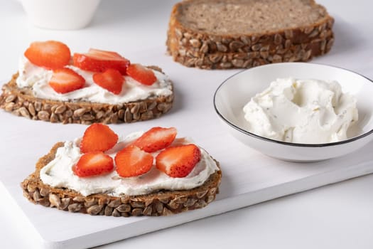 Rye bread with cream cheese and strawberry on a white table. Whole grain rye bread with seeds.