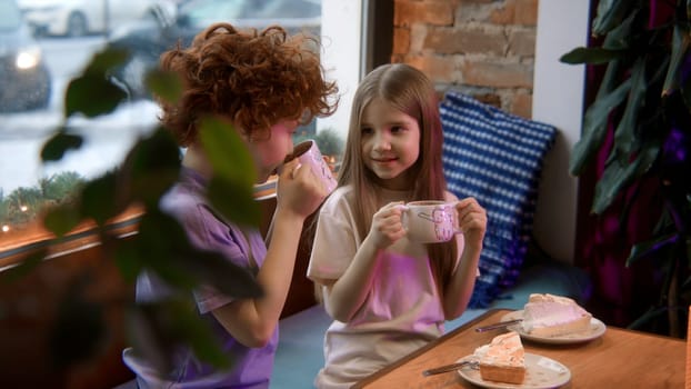 Boy and girl children eating cakes and drinking milk at the restaurant. Stock footage. Kids communicating and heaving desserts