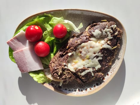 Baked meat with cheese, bacon slices, cherry tomatoes and lettuce, keto breakfast, view from above