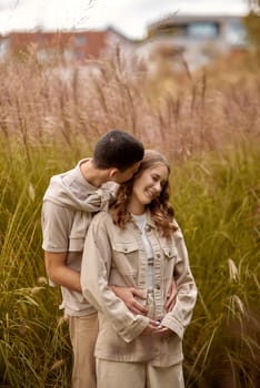 Happy couple on autumn walk outdoors. Two lovers in autumn park. Love and tender touch. Gentle hugs. Young man and woman in classic autumn colors outfit on a romantic date in a park. Young girl and guy with blond hair kisses, show love, affection. Boy and girl of European appearance with warm clothes, pictures with soft background bokeh blur fall. Concept of happiness,