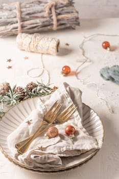 Christmas table with white plates, golden cutlery and holiday decorations.