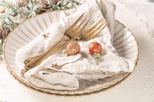 Christmas table with white plates, golden cutlery and holiday decorations.