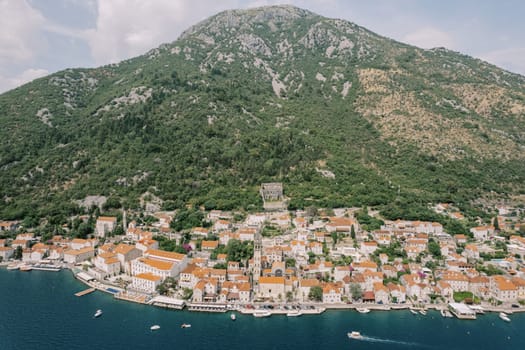 Bell tower of the Church of St. Nicholas among the red roofs of old houses on the shore of the bay. Perast, Montenegro. Drone. High quality photo