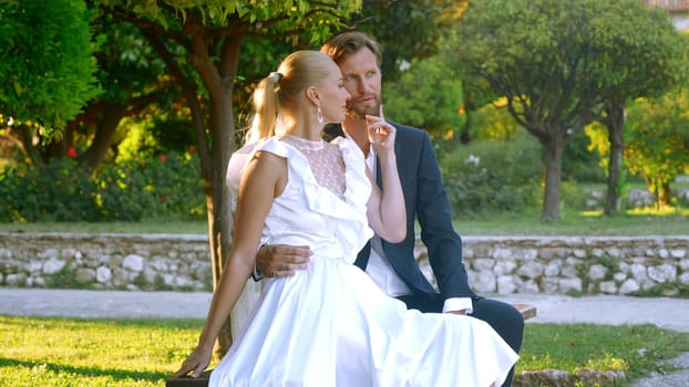 Beautiful bride with groom in a city park on a green blurred background. Action. Man and woman newlyweds during video shooting outdoors