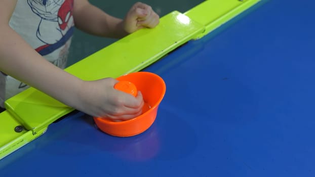 Close-up of child playing air hockey. Clip. Child plays air hockey in shopping mall with slot machines. Entertaining table air hockey for children.