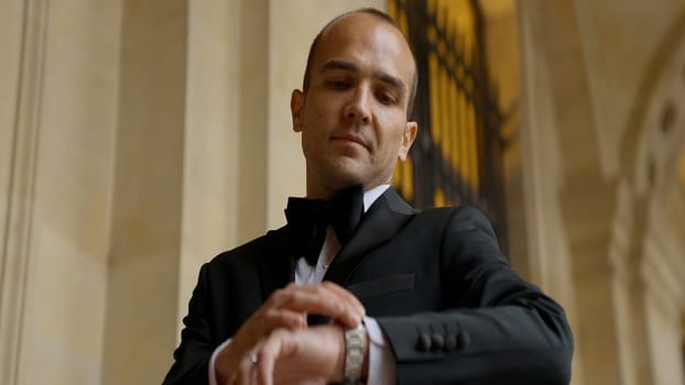 Low angle view of a man looking at his watch on the background of an ancient building. Action. Elegant man in suit