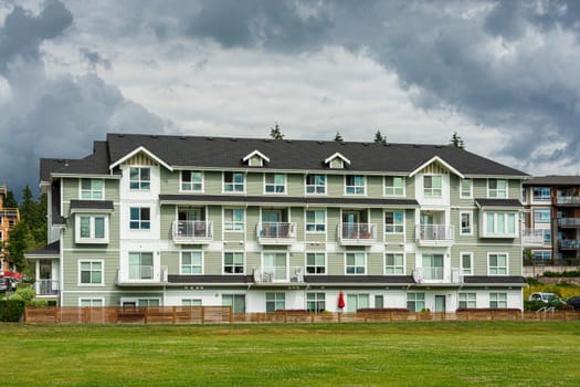 New residential low-rise building with big green lawn in front on cloudy sky background