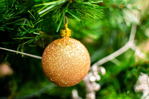 Golden bauble among chistmas tree brenches. Closeup look of the ball