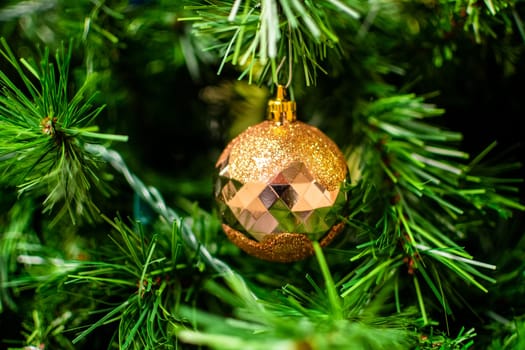 Golden bauble among chistmas tree brenches. Closeup look of the ball