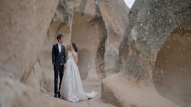 Photo shoot of the newlyweds in nature. Action. A cute couple in wedding costumes in the mountains posing for a photo session and it's snowing. High quality 4k footage