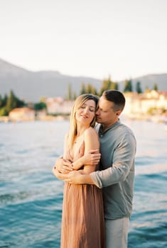 Man hugs woman from behind while standing on the seashore. High quality photo