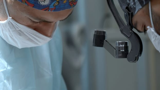 A close up male medical worker with a disposable mask and hat is wearing a special equipment on his head. Action. Surgeon at work in modern clinic