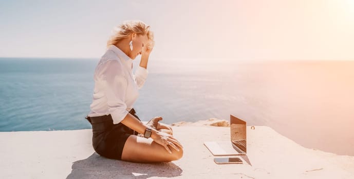 Happy girl doing yoga with laptop working at the beach. beautiful and calm business woman sitting with a laptop in a summer cafe in the lotus position meditating and relaxing. freelance girl remote work beach paradise