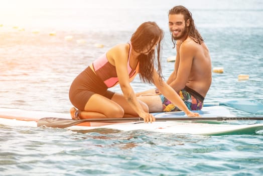 Sea woman and man on sup. Silhouette of happy young woman and man, surfing on SUP board, confident paddling through water surface. Idyllic sunset. Active lifestyle at sea or river