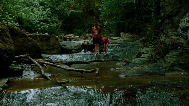 People walking barefeet in rocky mountainous river. Creative Summer hiking, cold stream in forest