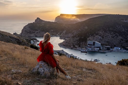 Woman sunset sea mountains. Happy woman siting with her back on the sunset in nature summer posing with mountains on sunset, silhouette. Woman in the mountains red dress, eco friendly, summer landscape active rest.