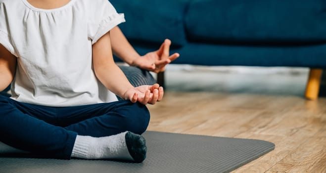 A mother and her daughter find joy in family yoga sitting in lotus position and focusing on mindfulness and meditation creating a harmonious and joyful family moment at home.