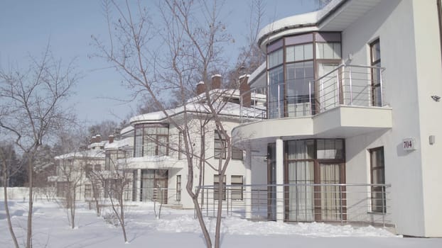 Winter landscape with cottages standing in a row of white color on the background of blue sky. Stock footage. Modern beautiful houses in snowy winter