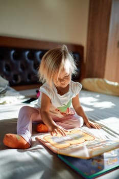 Little girl sitting on bed looking at picture book. High quality photo