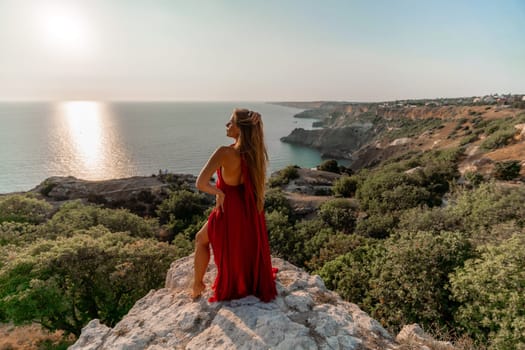 Woman sunset sea red dress, back view a happy beautiful sensual woman in a red long dress posing on a rock high above the sea on sunset