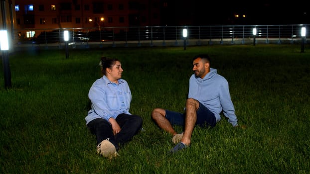 A man and a woman on a lawn in a city park looking happy while talking. Media. The concept of a family weekend and walks in the park