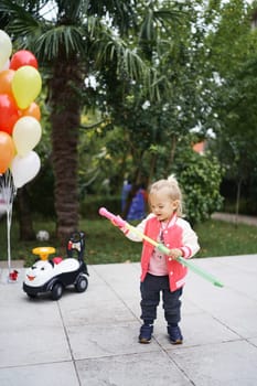 Little girl takes out a toy sword from a scabbard while standing in the garden next to a bunch of balloons. High quality photo